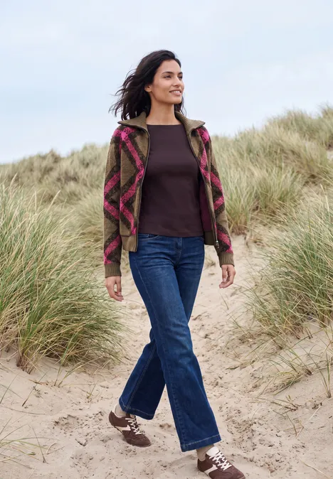 Federgarn Cardigan mit Troyerkragen pink flash Frau in Musterjacke und Jeans spaziert lächelnd über sandige Dünen