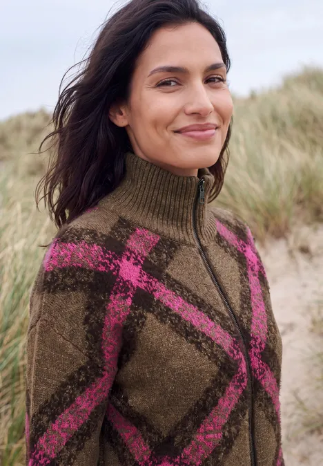 Federgarn Cardigan mit Troyerkragen pink flash Frau am Strand in einem braunen Wollpullover mit pinkem Karomuster und Reißverschluss.