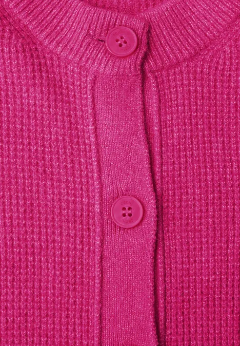 Nahaufnahme einer pinken, grob gestrickten Strickjacke mit Rippenmuster und rosa Knöpfen