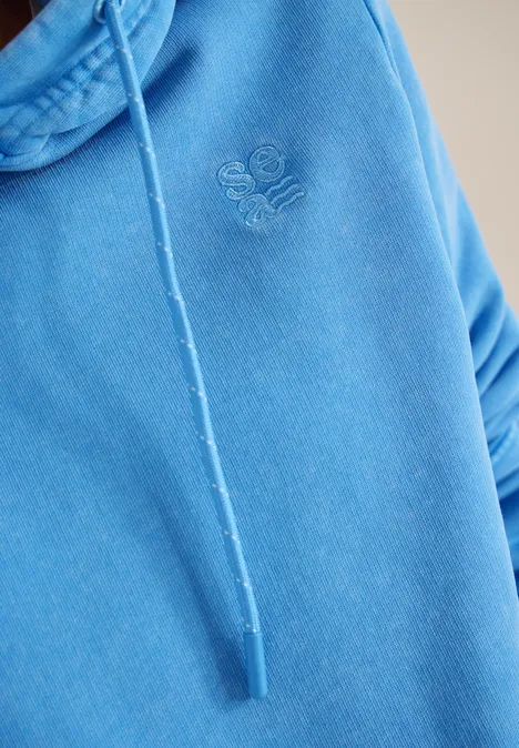 Hoodie mit Stickerei fountain blue Nahaufnahme eines blauen Kapuzenpullovers mit Kordelzug und dezentem aufgesticktem Emblem auf der Brust.