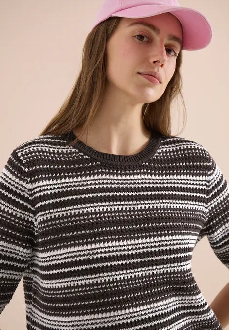 Eine Frau trägt einen schwarz-weiß gestreiften Strickpullover und eine rosa Baseballkappe.
