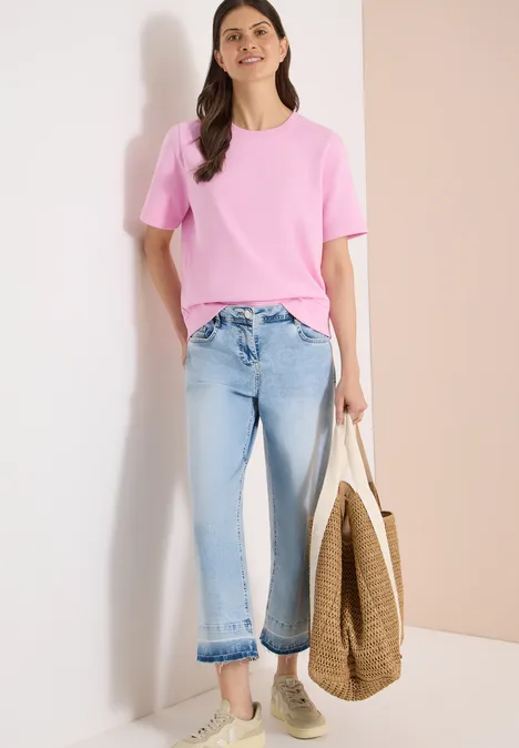 Sweater met korte mouwen en ronde hals light blush rose Een persoon draagt een roze T-shirt, lichtblauwe jeans en heeft een gevlochten tas, gecombineerd met sneakers.