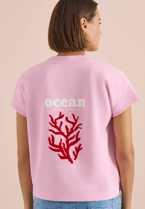 Sweater met korte mouwen en rugprint light blush rose Vrouw van achteren in roze t-shirt met 'ocean'-tekst en rood koraalmotief