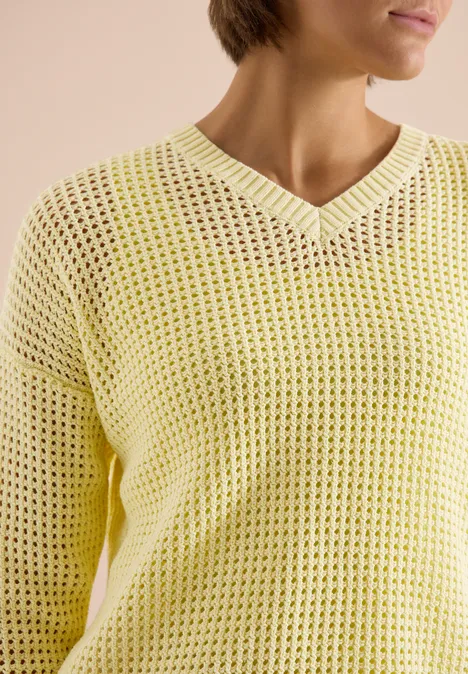 Nahaufnahme einer Person in einem gelben, locker gestrickten V-Ausschnitt-Pullover.