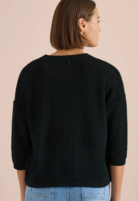 Achteraanzicht van een persoon in een zwarte grofgebreide trui met driekwartmouwen voor een beige achtergrond