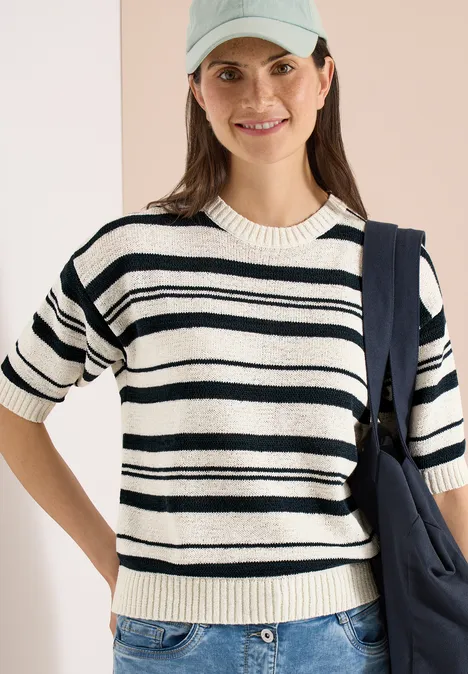 Femme portant un T-shirt à manches courtes crème à rayures foncées et un sac en bandoulière.