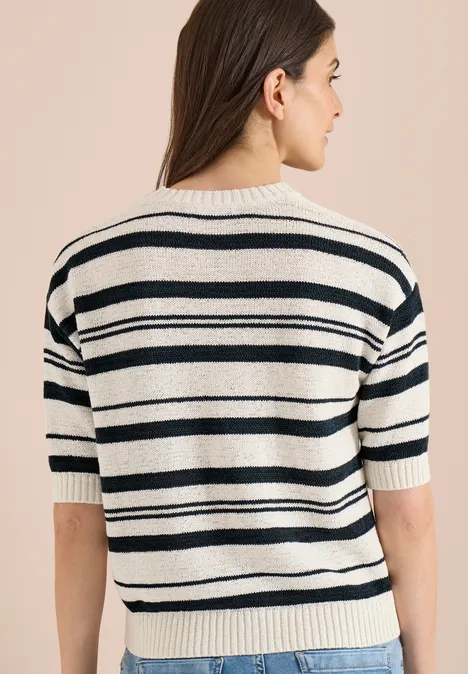 Vue de dos d'une personne portant un pull fin à manches courtes blanc à rayures noires sur fond beige.