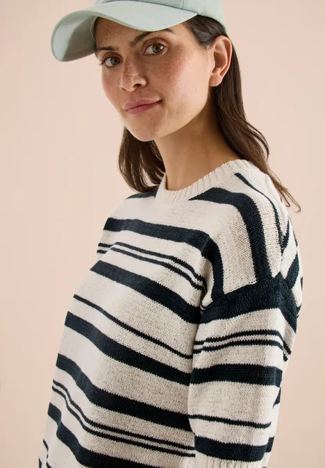 Femme portant une casquette et un pull rayé noir et blanc, avec une boucle d’oreille visible