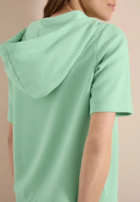 Dame in mintgrüner, kurzärmeliger Kapuzenjacke aus strukturiertem Stoff, Rückansicht.