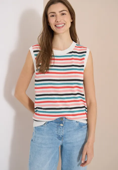 Femme en top sans manches à rayures colorées et jean devant un fond neutre.