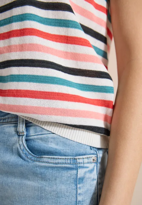 Gros plan sur une personne portant un haut rayé pastel et un jean bleu clair.