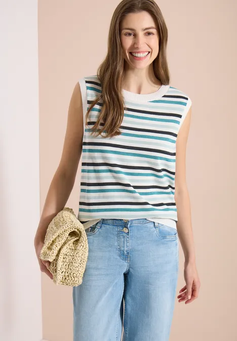 Femme portant un top sans manches rayé, un jean bleu clair et un sac en paille.