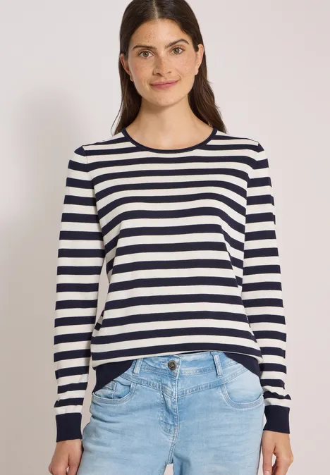Trui met ronde hals en strepen urban dark blue Jonge vrouw in een gestreepte longsleeve en spijkerbroek, glimlacht voor een witte achtergrond.