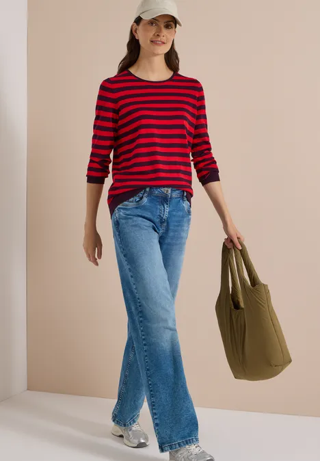 Trui met ronde hals en strepen eggplant red Vrouw in rood-zwarte trui, wijde jeans, pet en groene tas.