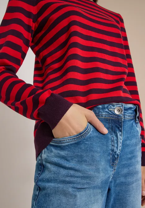 Trui met ronde hals en strepen eggplant red Rode trui met zwarte strepen en lange mouwen, blauwe jeans, hand in zak.