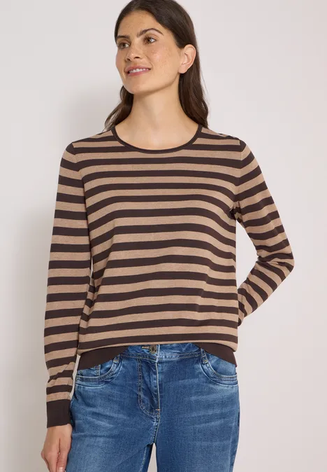 Trui met ronde hals en strepen truffle brown Vrouw in beige-zwart gestreepte trui en blauwe jeans, half glimlachend voor een lichte achtergrond.
