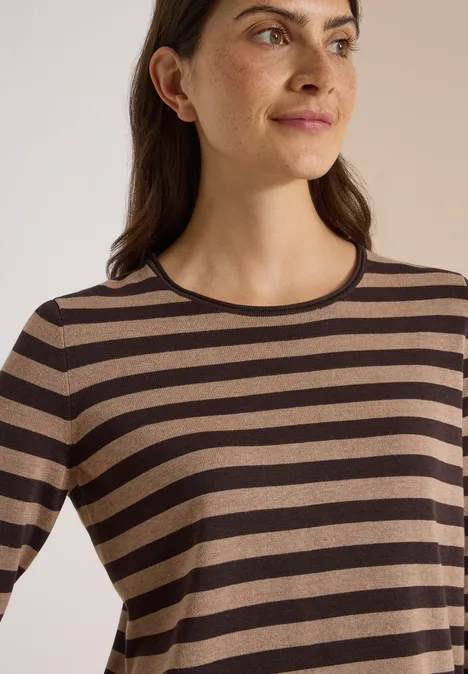 Trui met ronde hals en strepen truffle brown Vrouw met bruin-zwart gestreept shirt met lange mouwen, kijkt opzij.