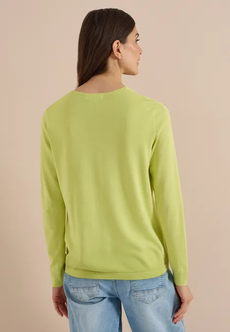 Pull basique à col rond citrin green Rückansicht einer Person mit hellem Grünpullover und blauen Jeans vor beigem Hintergrund.