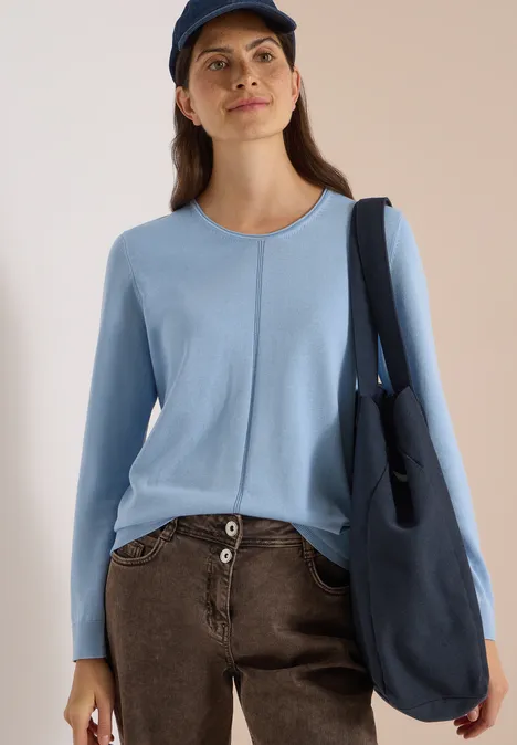 Basic Pullover mit Rundhals easy blue Frau trägt hellblauen Pullover, braune Hose, blaue Umhängetasche und Mütze.