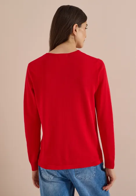 Basic Pullover mit Rundhals flame red Frau von hinten mit rotem Langarmshirt, blauen Jeans vor beigem Hintergrund.
