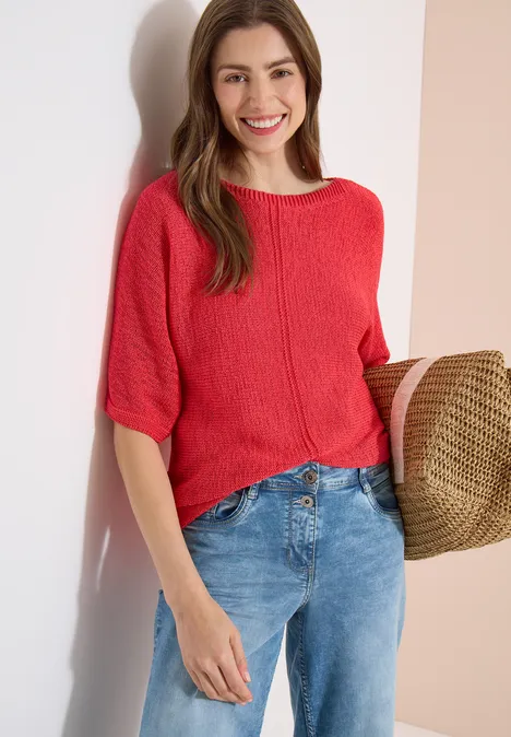Dolman Pullover mit U-Boot-Ausschnitt coral Frau in rotem Strickshirt, Jeans und Strohhut in der Hand.