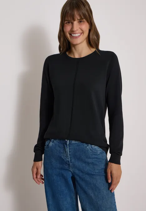 Basic Pullover mit Rundhals in Unifarbe Black Frau mit schwarzem Langarmshirt und blauen Jeans, die lächelnd in die Kamera schaut.