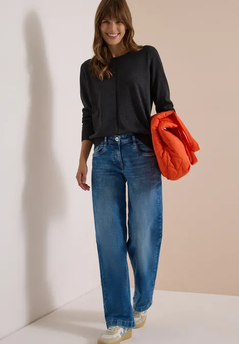Basic Pullover mit Rundhals in Unifarbe charcoal grey melange Fröhliche Frau mit schwarzem Langarmshirt und blauen Jeans hält eine orangefarbene Steppjacke im Arm.