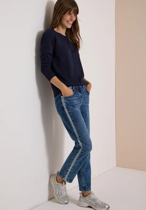 Basic Pullover mit Rundhals in Unifarbe urban dark blue Frau lehnt lässig in Jeans, dunkelblauem Pullover und Sneakern an einer Wand und lächelt.
