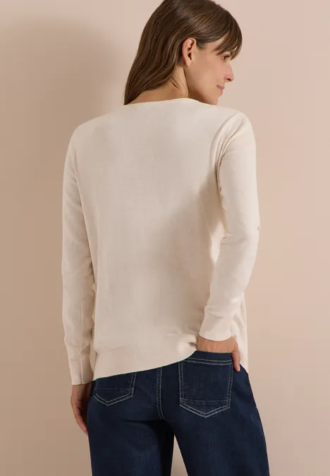 Basic Pullover mit Rundhals in Unifarbe oat milk beige melange Eine Frau von hinten in einem hellbeigen Langarmpullover und blauer Jeans vor hellem Hintergrund.