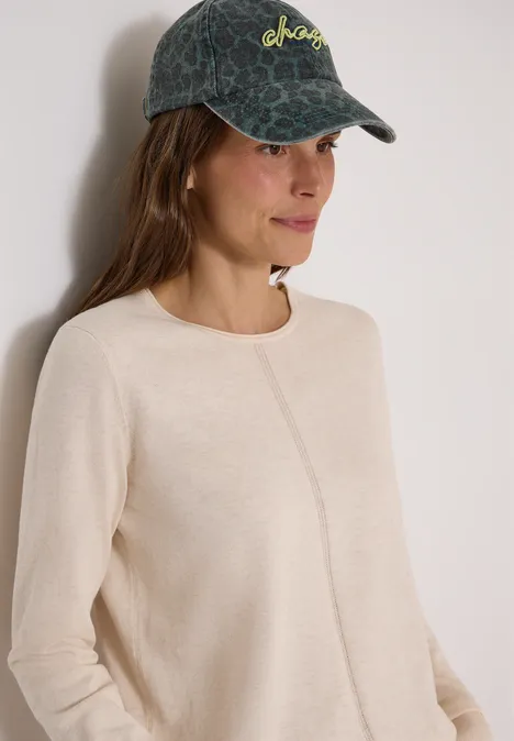 Basic Pullover mit Rundhals in Unifarbe oat milk beige melange Eine junge Frau trägt einen hellbeigen Pullover mit mittiger Naht und eine dunkelgrüne Cap mit Muster.
