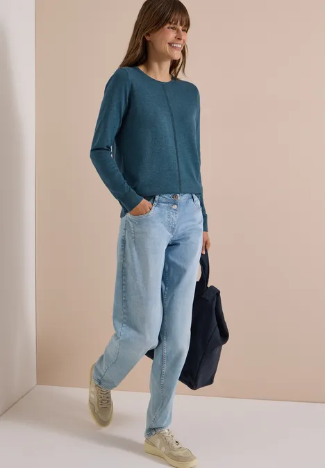 Basic Pullover mit Rundhals in Unifarbe dull teal blue melange Eine Frau in locker sitzender Jeans, tealfarbenem Pullover und hellen Sneakern, die lächelnd eine Jacke hält.
