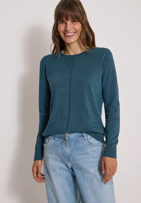Basic Pullover mit Rundhals in Unifarbe dull teal blue melange Eine lächelnde Frau in einem petrolfarbenen Langarmshirt und hellen Jeans vor neutralem Hintergrund.