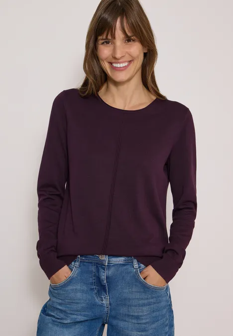 Basic Pullover mit Rundhals in Unifarbe eggplant red Frau mit violettem Pullover und Jeans, lächelnd mit Händen in den Taschen vor hellem Hintergrund.