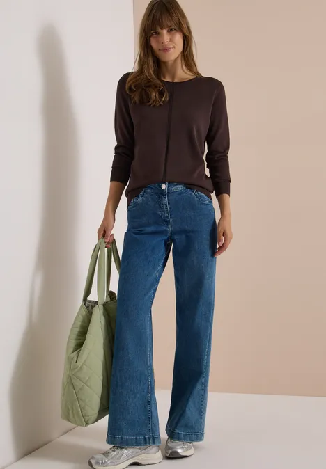 Basic Pullover mit Rundhals in Unifarbe truffle brown Eine Frau vor einer Wand in weiten blauen Jeans, dunkelbraunem Top, Sneakern und mit großer grüner Umhängetasche.