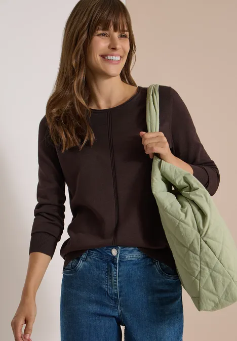 Basic Pullover mit Rundhals in Unifarbe truffle brown Frau in braunem Pullover und Jeans trägt lächelnd eine hellgrüne, gesteppte Tasche über der Schulter.