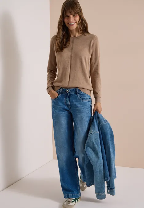 Basic Pullover mit Rundhals in Unifarbe creamy mocha melange Frau im beigen Cardigan und weiten Jeans, hält eine Jeansjacke in der Hand vor hellem Hintergrund.