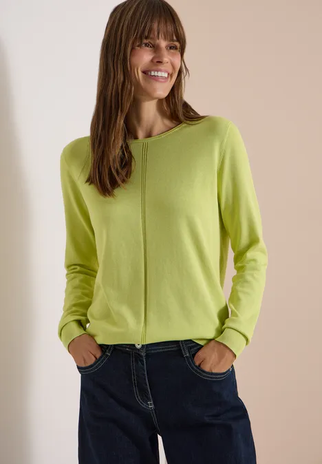 Basic Pullover mit Rundhals in Unifarbe citrin green Eine lächelnde Frau trägt einen hellgrünen Pullover und dunkle Jeans vor neutralem Hintergrund.
