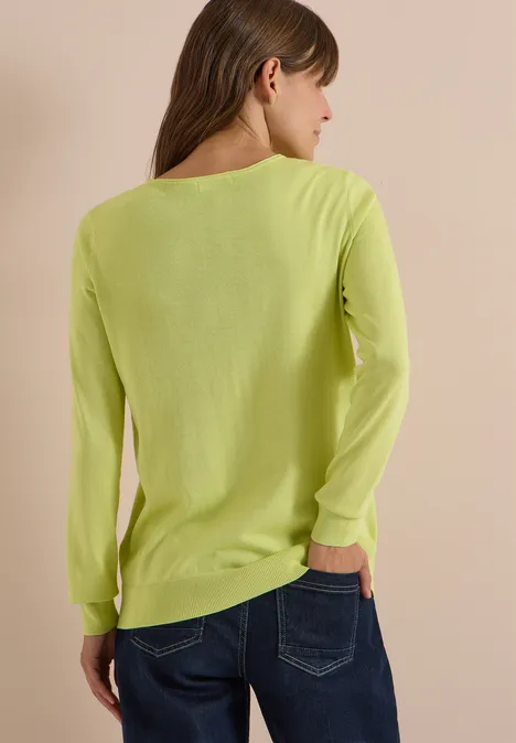 Basic Pullover mit Rundhals in Unifarbe citrin green Frau von hinten in neongelbgrünem Langarmshirt und blauen Jeans vor beigem Hintergrund.
