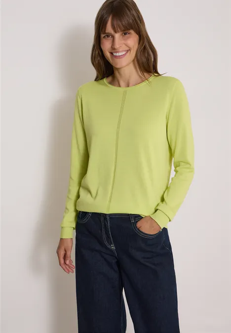 Basic Pullover mit Rundhals in Unifarbe citrin green Frau im grünen Pullover und blauen Jeans, lächelnd vor hellem Hintergrund.