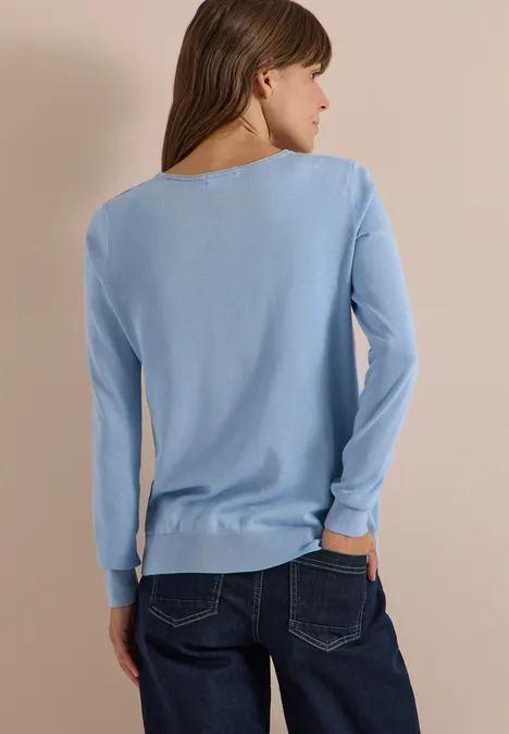 Basic Pullover mit Rundhals in Unifarbe easy blue Frau von hinten in hellblauem Langarm-Pullover und Jeans vor beigem Hintergrund.