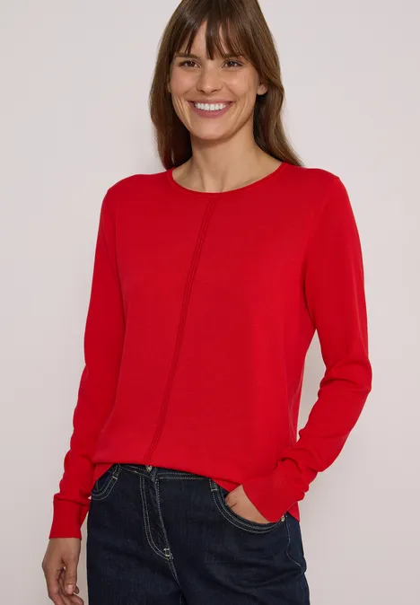 Basic Pullover mit Rundhals in Unifarbe flame red Eine lächelnde Frau in rotem Pullover und Jeans vor hellem Hintergrund.