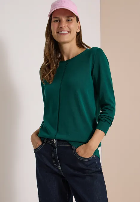 Basic Pullover mit Rundhals in Unifarbe dark fir green Junge Frau in grünem Pullover, Jeans und rosa Mütze, die lächelnd die Hände in den Taschen hält