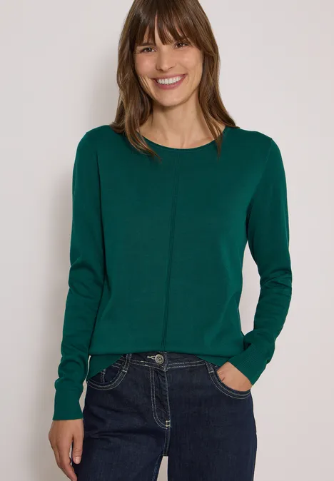 Basic Pullover mit Rundhals in Unifarbe dark fir green Junge Frau in grünem Pullover und Jeans lächelt in die Kamera.