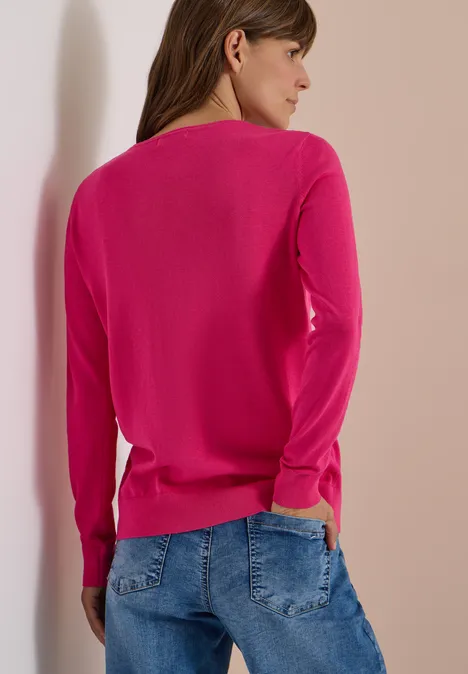 Basic Pullover mit Rundhals in Unifarbe pink flash Frau von hinten in pinkem Pullover und blauer Jeans, lehnt an einer hellen Wand.