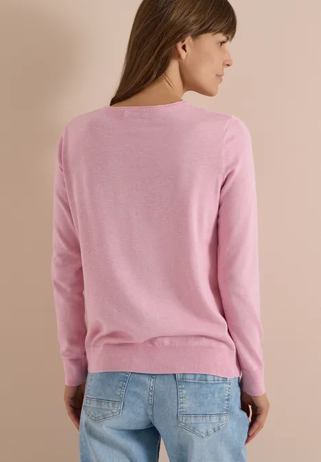 Frau von hinten in rosa Pullover und Jeans vor beigem Hintergrund.