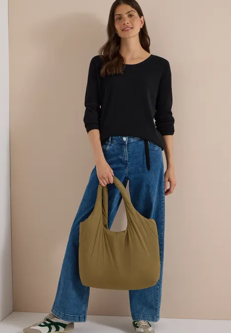Frau in schwarzem Pullover und blauen Jeans hält olivgrüne Hobo-Tasche.