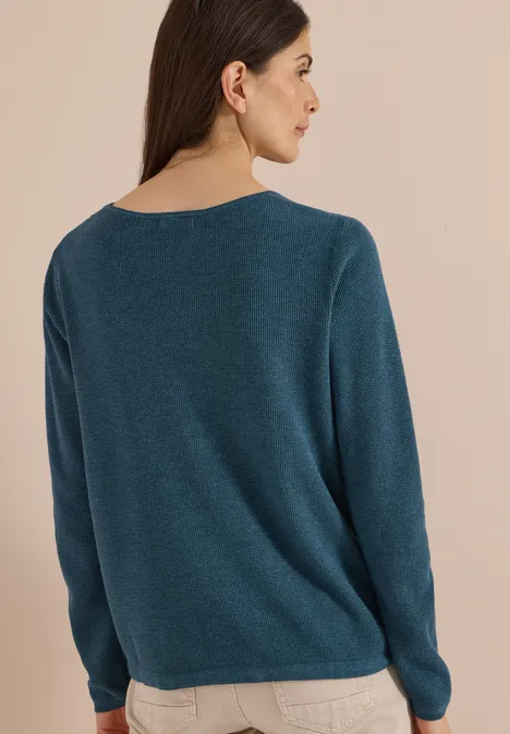 Eine Frau ist von hinten zu sehen und trägt einen schlichten, blauen Pullover.