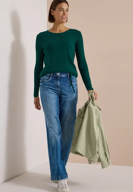 Pullover mit Rundhals und Struktur dark fir green Frau in grünem Langarmshirt und Jeans hält hellgrüne Jacke, steht vor neutralem Hintergrund.