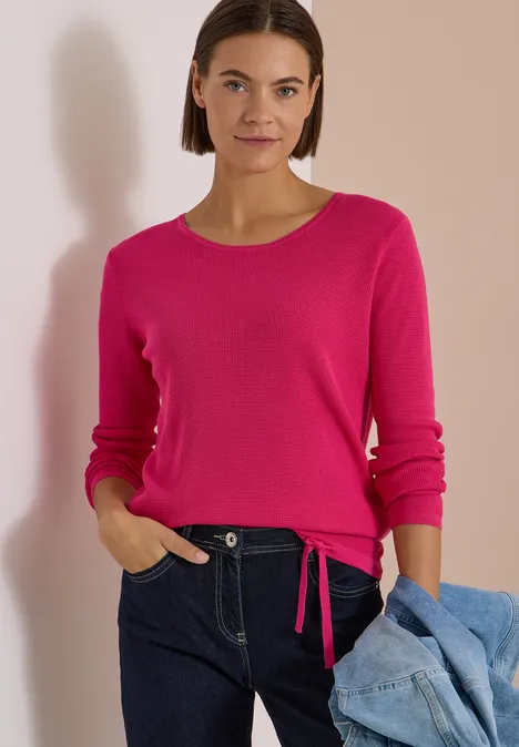 Pullover mit Rundhals und Struktur pink flash Frau in pinkem Pullover, dunkler Jeans, mit Jeansjacke vor beiger Wand.