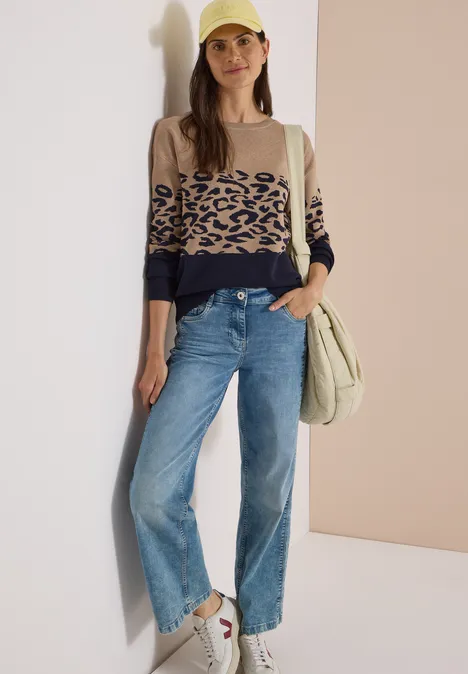Langarm Pullover mit Leo-Jacquard-Muster urban dark blue Frau in geraden Jeans, beigem Leo-Pullover und grüner Umhängetasche vor neutralem Hintergrund.